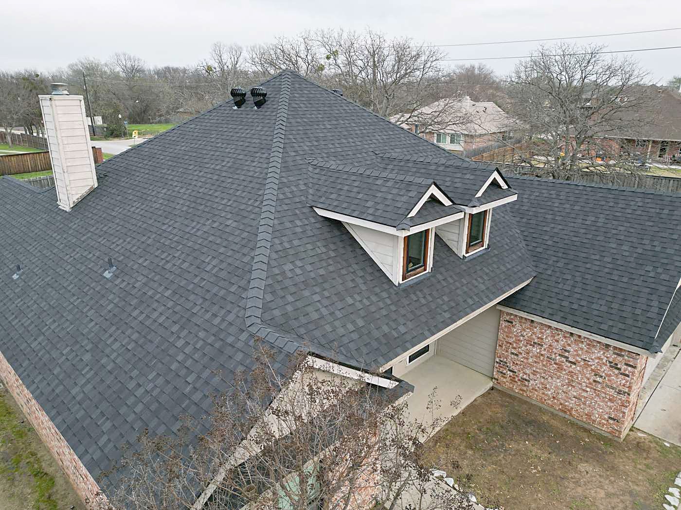 Aerial view of a brick home with two dormers and a new charcoal shingle roof