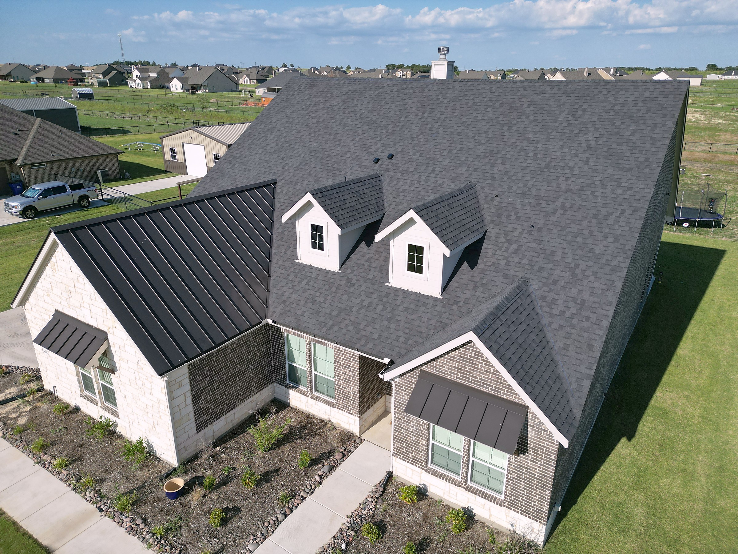 A brick and stone home with a new charcoal shingle roof, two dormers and standing seam metal over the porches