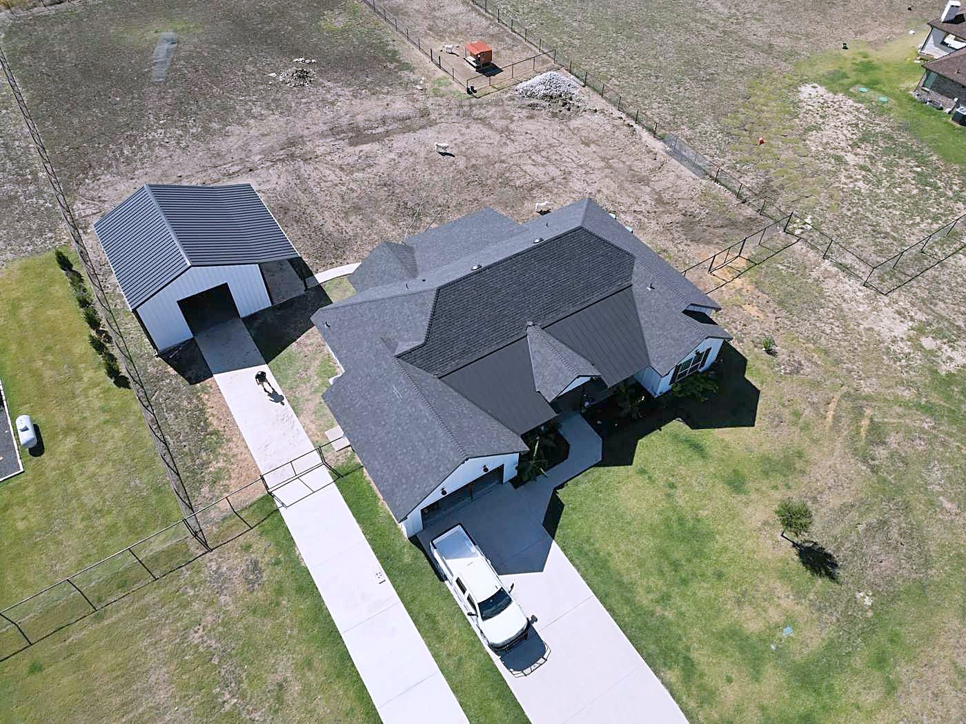 A home and detached workshop with new dark shingle roofs on a large lot