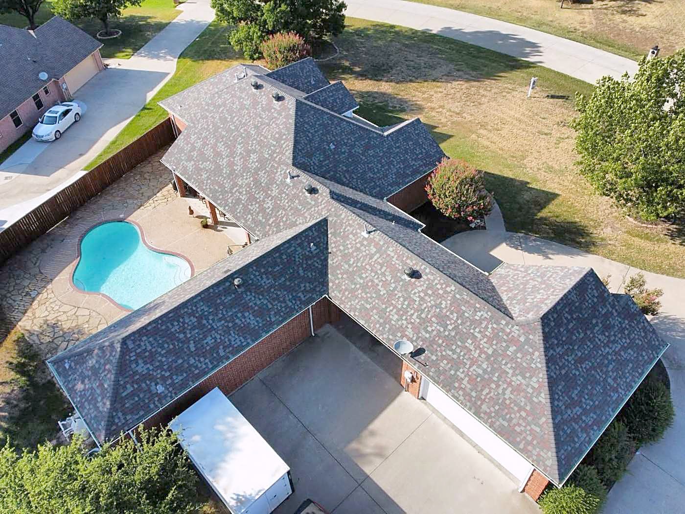 A brick home with a backyard pool under a newly finished blended-color shingle roof