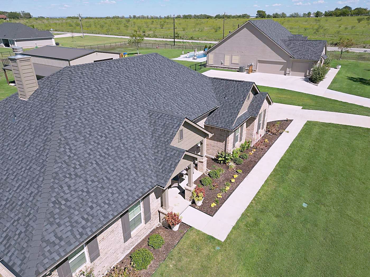 A brick and siding home with a new dark shingle roof beside an open field
