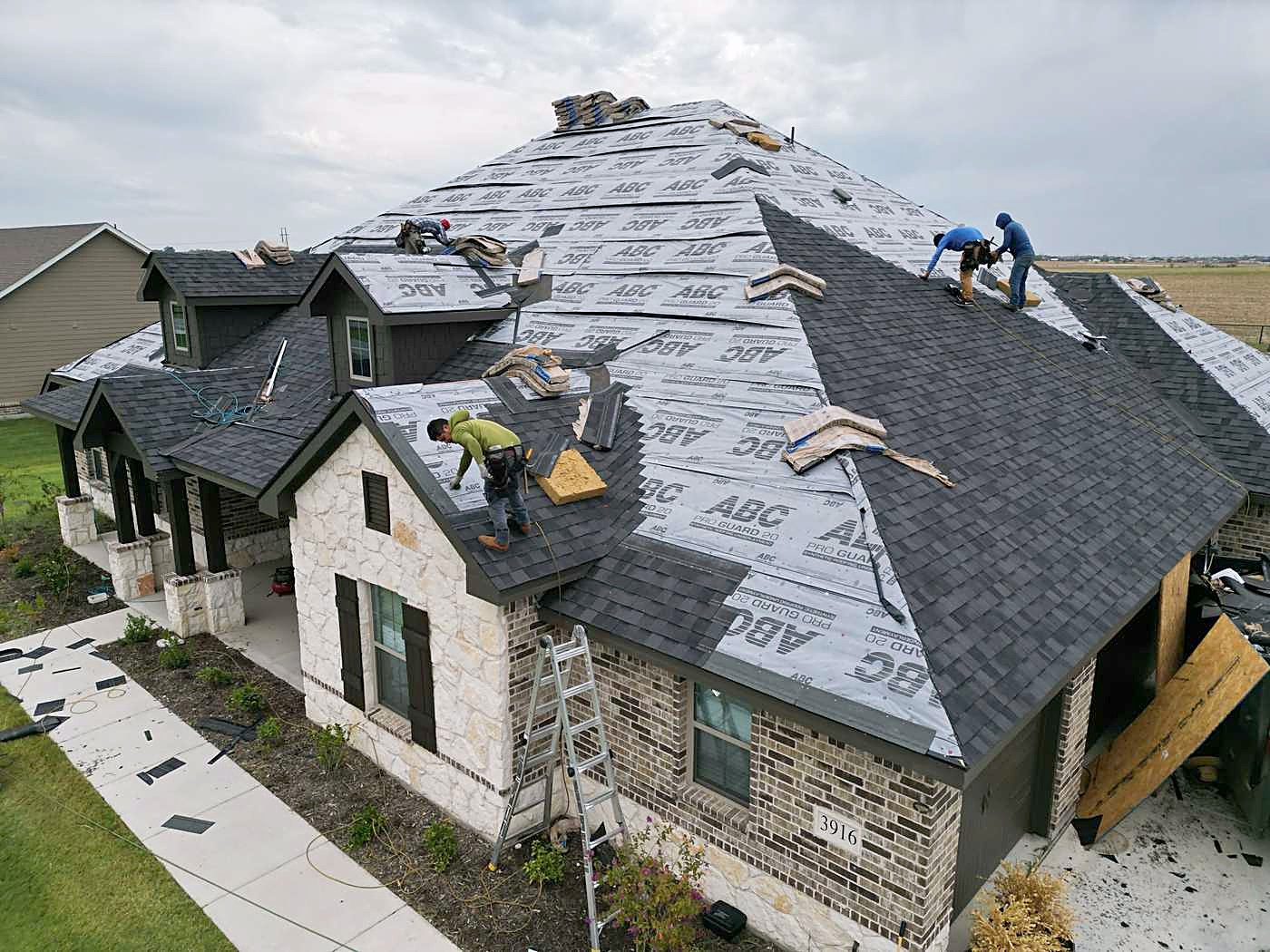 A roofing crew installing underlayment and shingles on a stone home