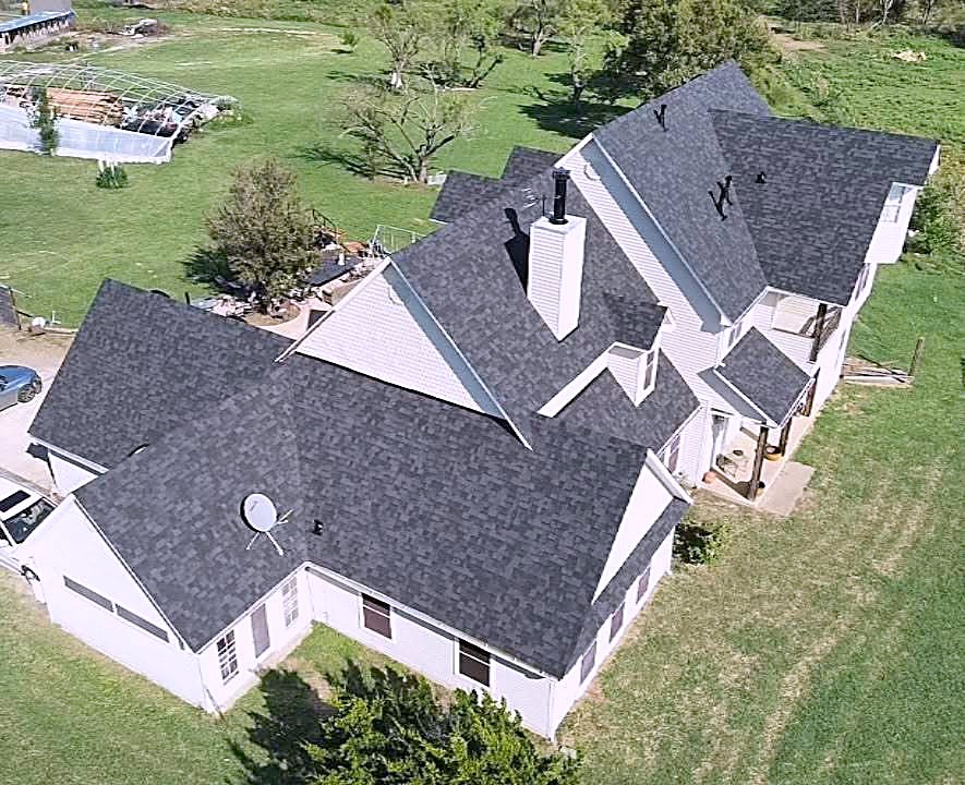 A white home with a charcoal shingle roof and a large green yard