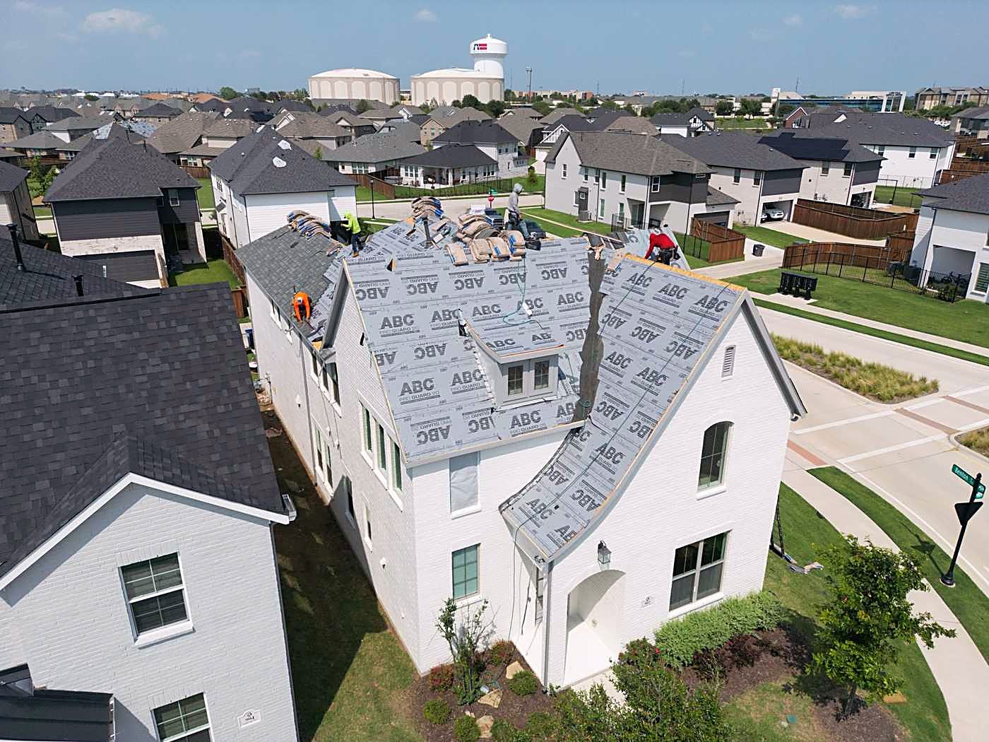 A white two-story home mid-replacement with synthetic underlayment on the upper roof